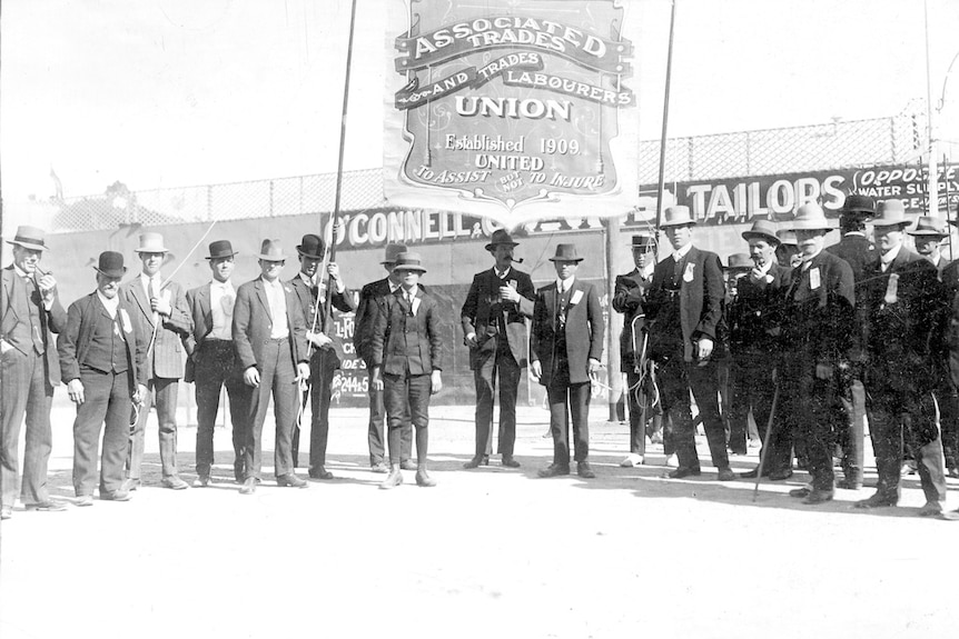 Trade union members stand in front of a banner.