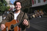 Aaron Pollock poses in the Bourke Street Mall holding his guitar