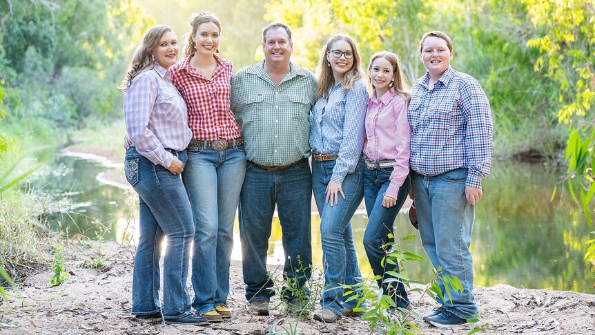 Family of six stand smiling at camera wearing rural shirts and jeans