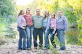 Family of six stand smiling at camera wearing rural shirts and jeans