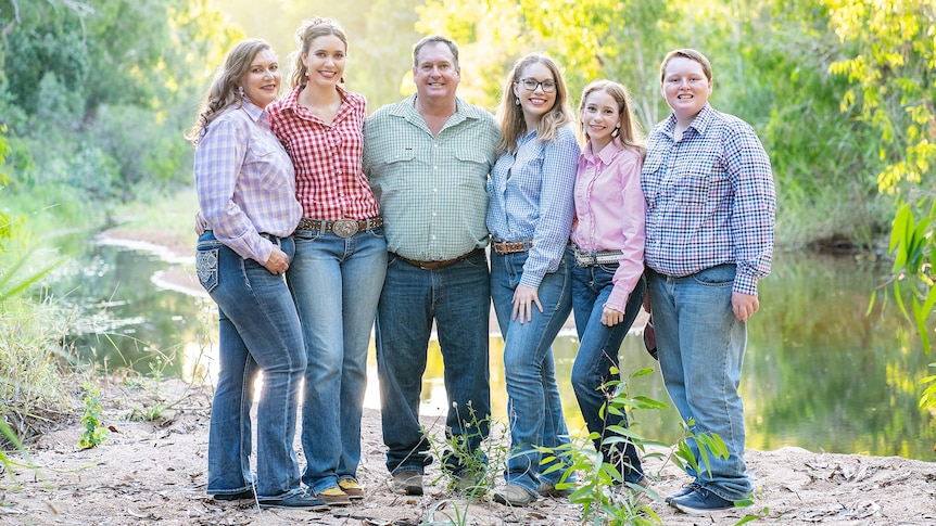 Family of six stand smiling at camera wearing rural shirts and jeans