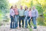 Family of six stand smiling at camera wearing rural shirts and jeans