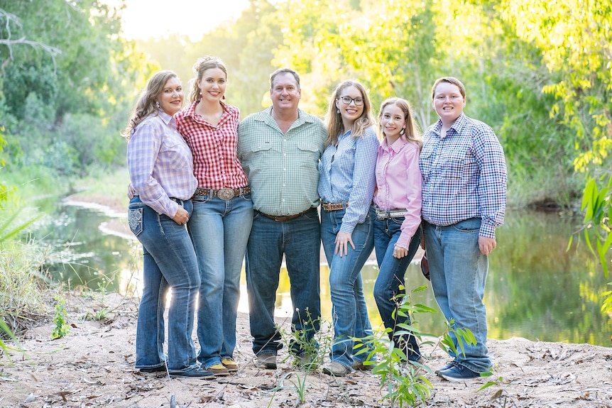 Family of six stand smiling at camera wearing rural shirts and jeans