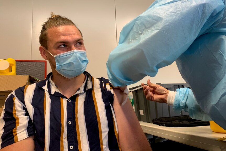 Daniel Hammond receives a COVID-19 vaccination from a nurse wearing blue PPE.