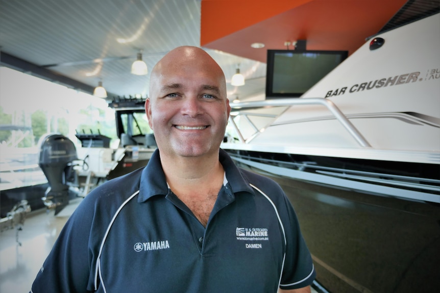 Man standing in navy branded polo shirt in a boat showroom.