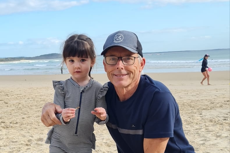 A smiling older man on a beach with a little girl.