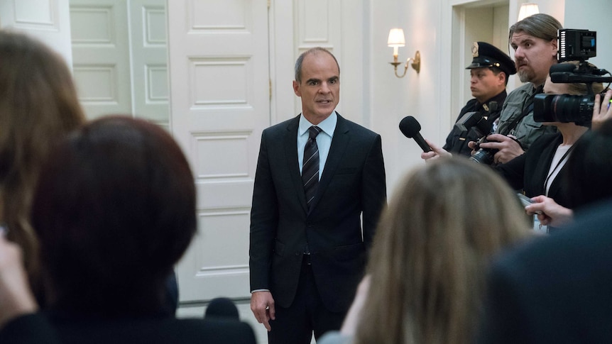 Actor Michael Kelly in a suit surrounded by reporters in a scene from TV show House of Cards