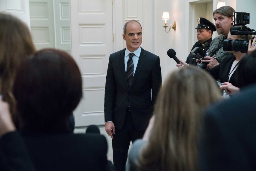 Actor Michael Kelly in a suit surrounded by reporters in a scene from TV show House of Cards