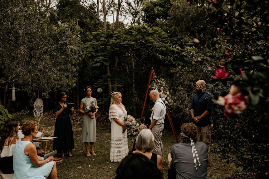 Une mariée et un marié face à face, l'autre tenant des fleurs.