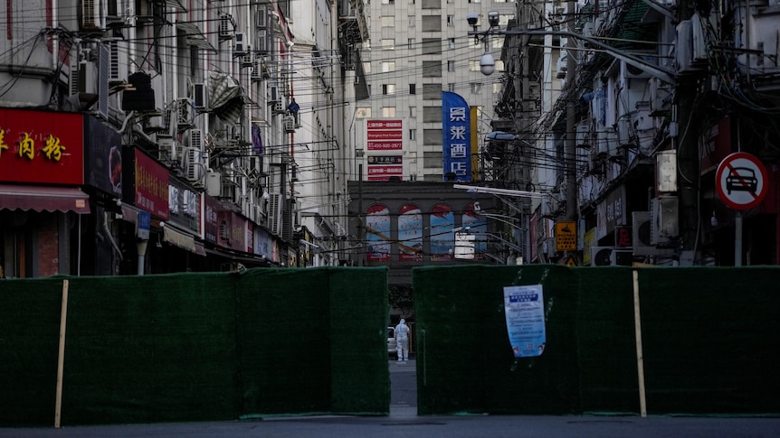 A worker in a protective suit is pictured behind barriers sealing off an area in a city. 