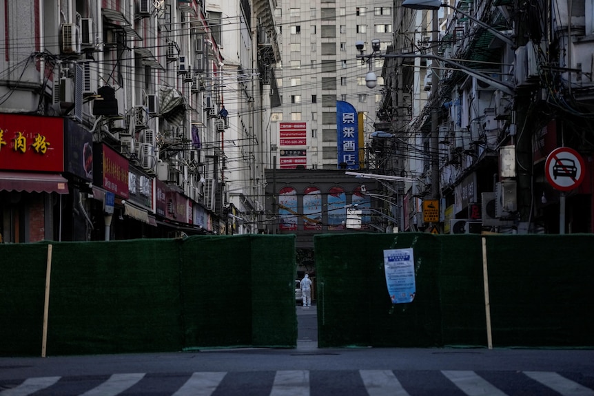 A worker in a protective suit is pictured behind barriers sealing off an area in a city. 