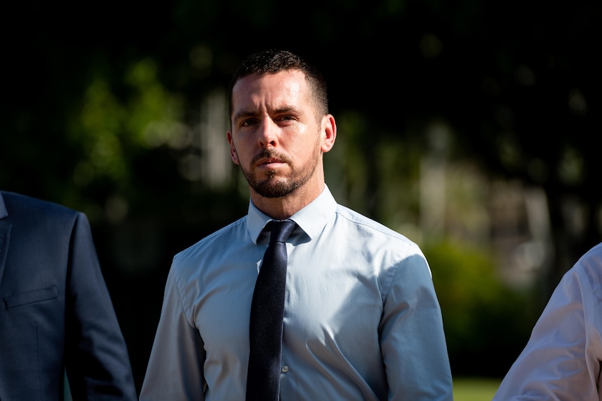 A man in a blue tie and business shirt with a serious expression walks outside. 