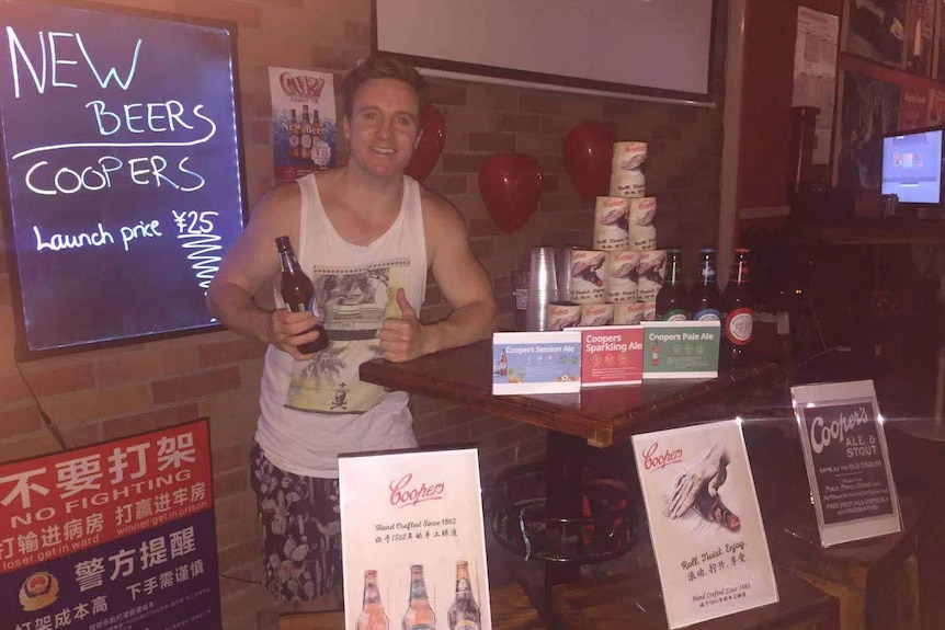 Melbournian entrepreneur Tyson Murphy holds a Coopers beer near a table at a bar.