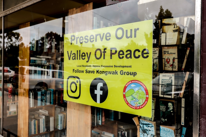 A yellow sign reading Preserve our Valley of Peace displayed in a shop window with books and clothes in background