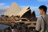 A man in a mask in front of a blurred opera house