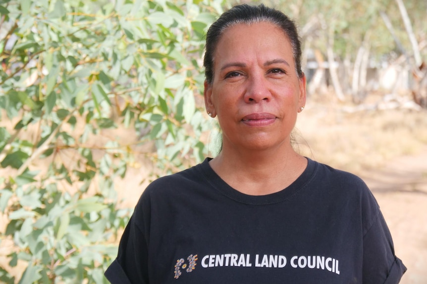 A woman wearing a black shirt with 'Central Land Council' written, looks at the camera with a serious expression.
