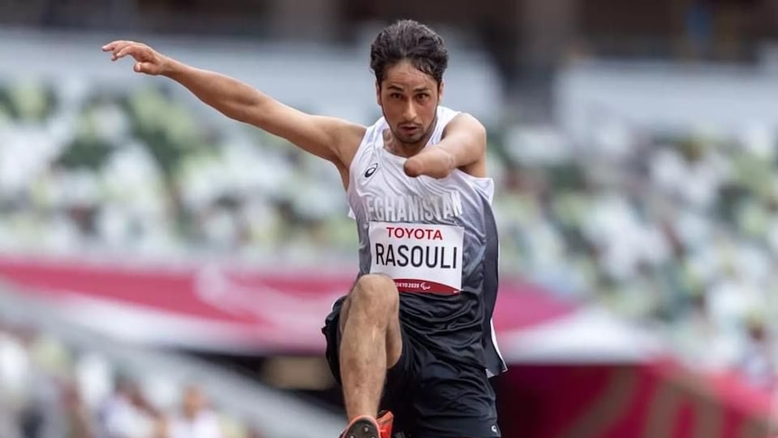 A disabled male athlete with partly amputated left arm and name Rasouli on his bib jumps in the air at stadium 