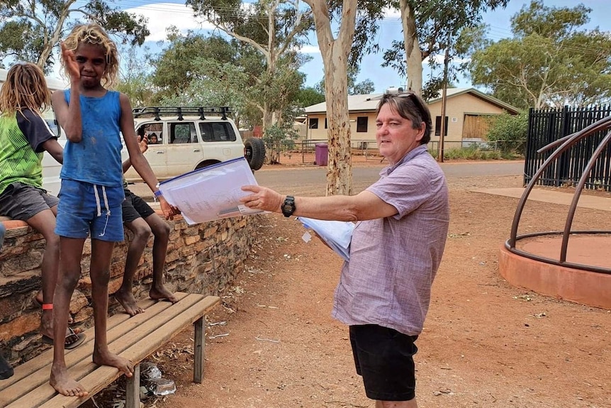 A man holding a white folder standing next to an Aboriginal child