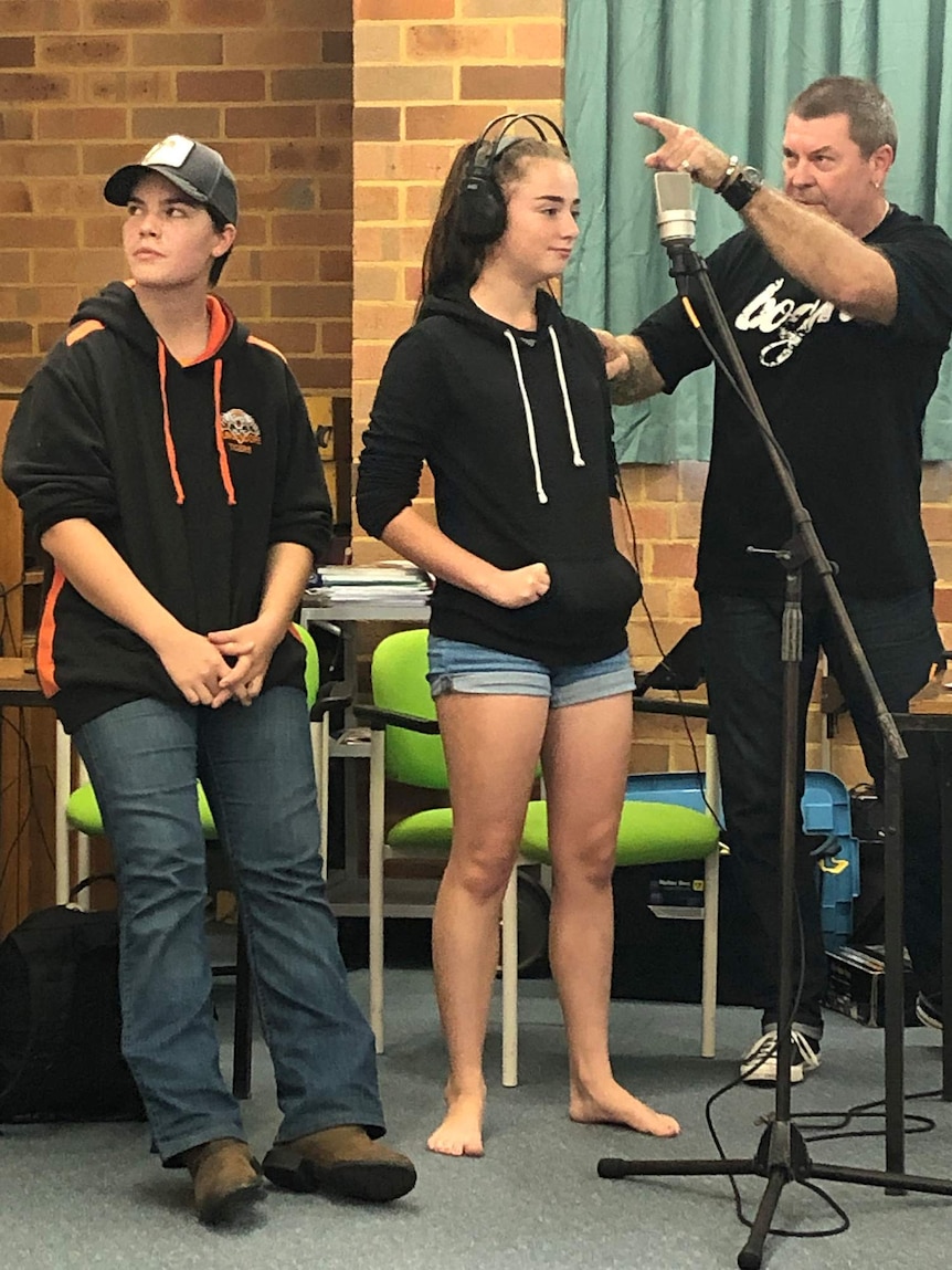 Two girls and a man standing in front of a microphone