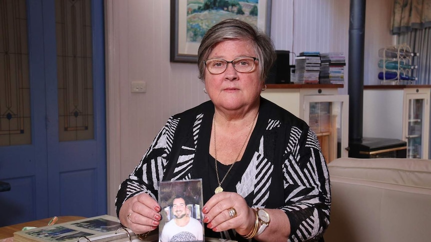 A woman sits at a table with a photo album, holding one picture.