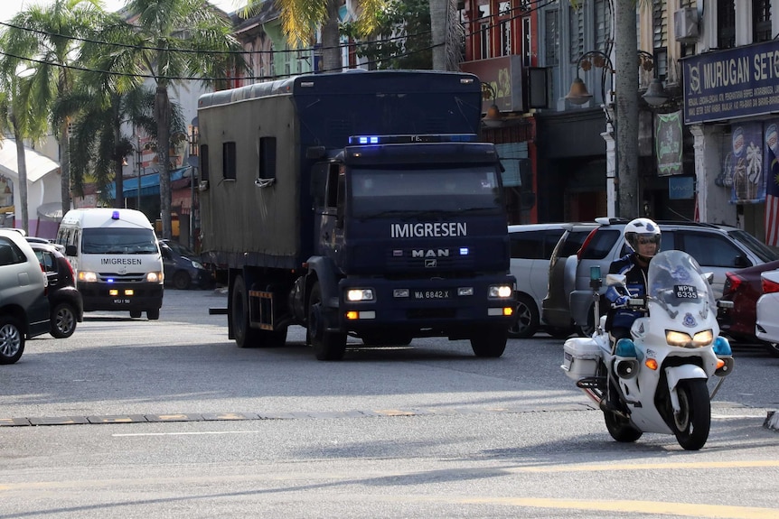 A police escort of a black immigration truck on a city street in tropical setting.