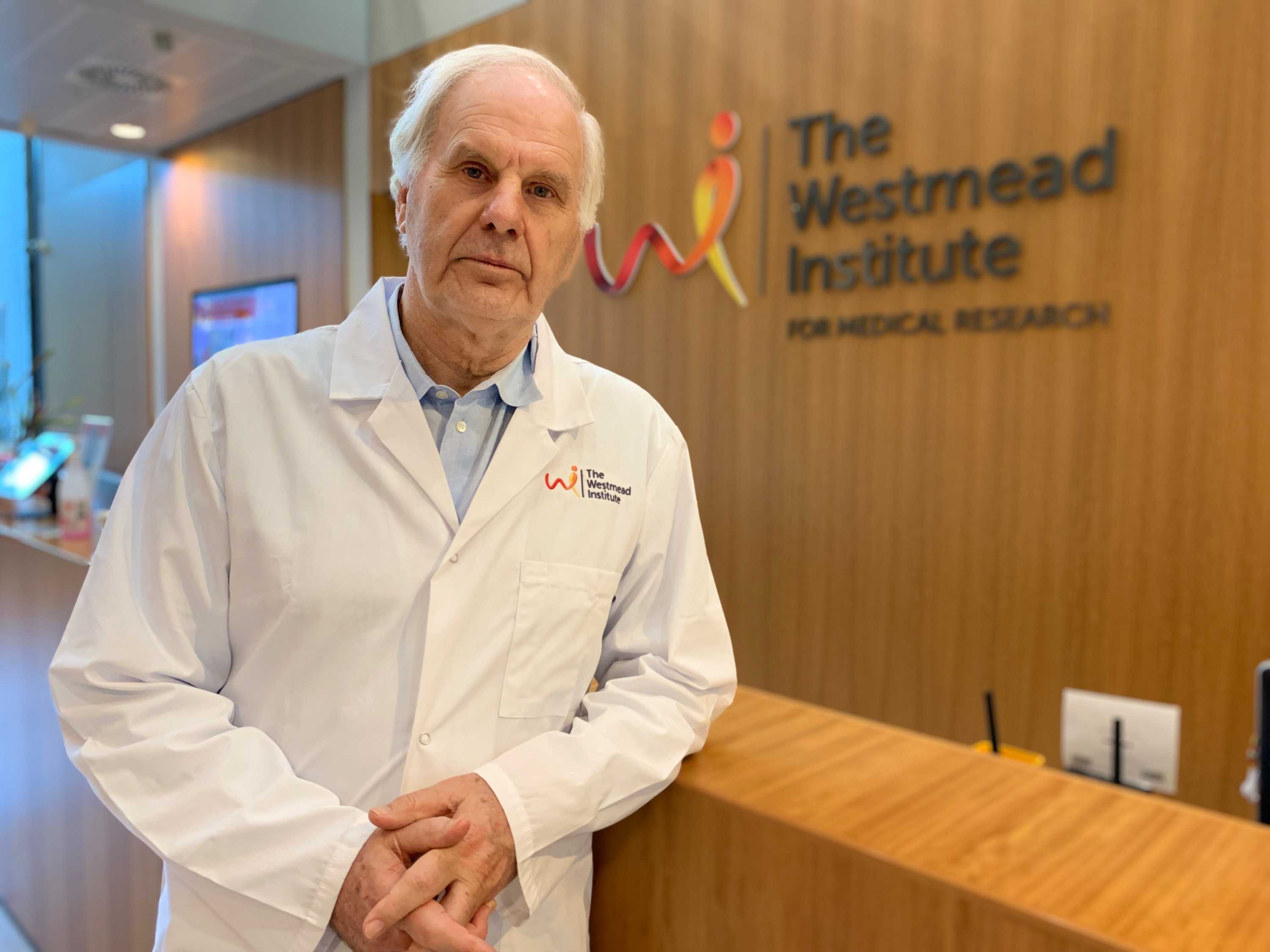 A man in a white coat standing in front of a sign.