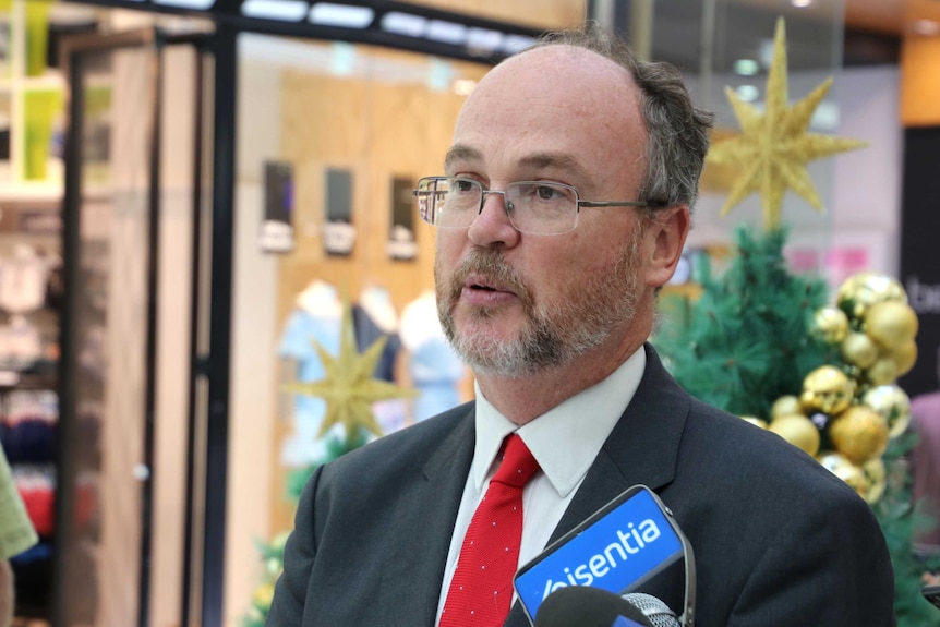 A man in a red tie at a shopping centre surrounded by Christmas decorations