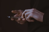 A hand holds a smartphone against a black background.