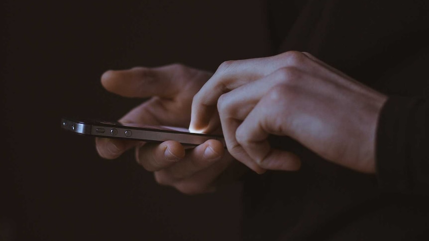 A hand holds a smartphone against a black background.