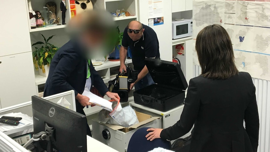 ASIO officer puts files into bag while cameraman films him.