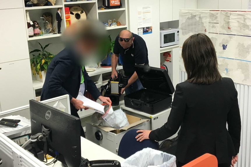 ASIO officer puts files into bag while cameraman films him.