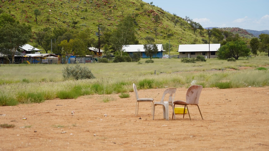 A few chairs and a table on a large patch of dirt in a rural community.
