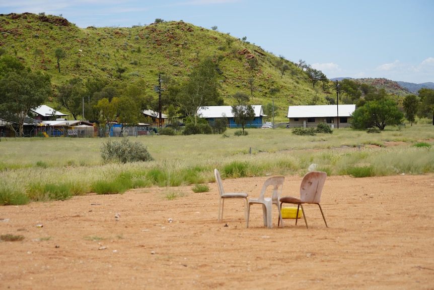 A few chairs and a table on a large patch of dirt in a rural community.