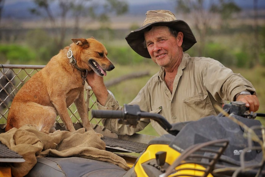 Farmer David Vonhoff pats his red heeler dog, who is sitting on the back of a quad bike.