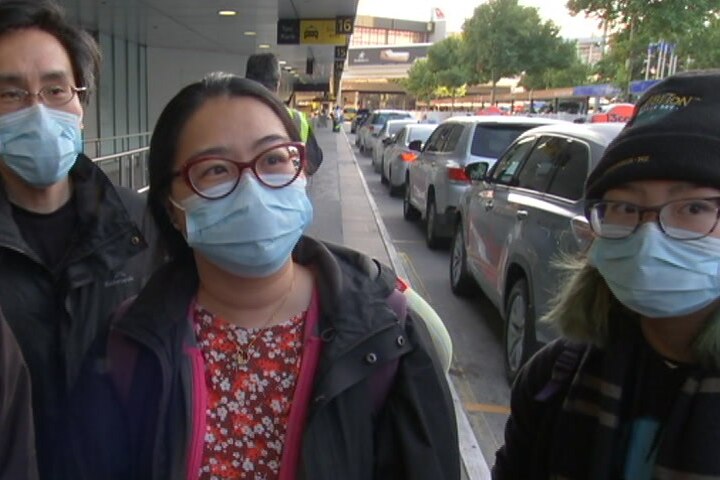Four people - two men, two women - wearing medical masks stand on the footpath outside the Melbourne airport.