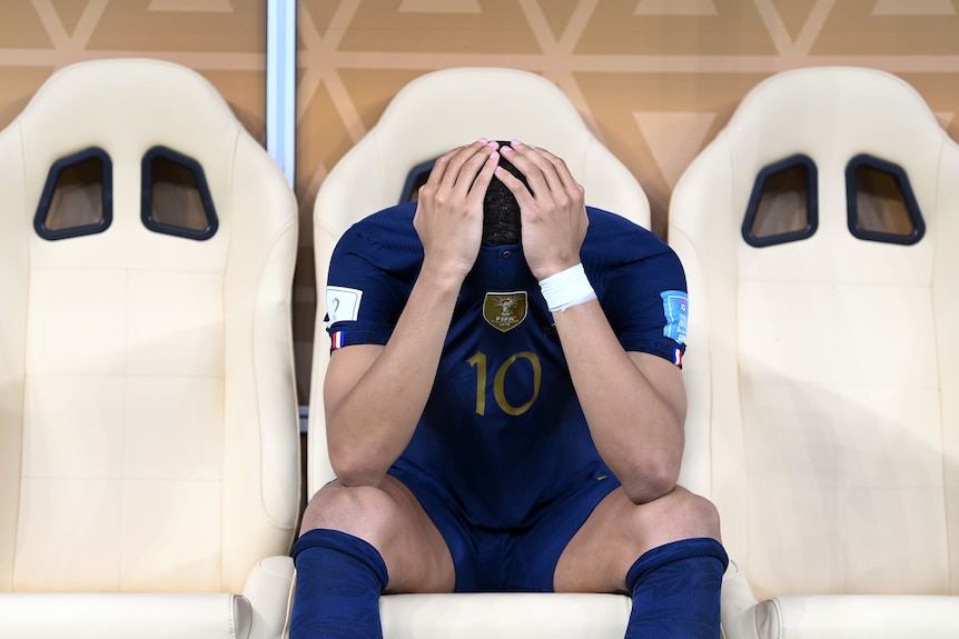 Kylian Mbappe holds his head with his face covered by his shirt