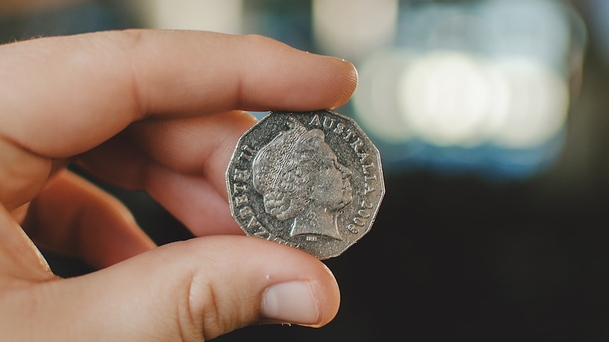 A hand holds up an Australian 10 cent coin between thumb and forefinger. The coin has the Queen's head on it.