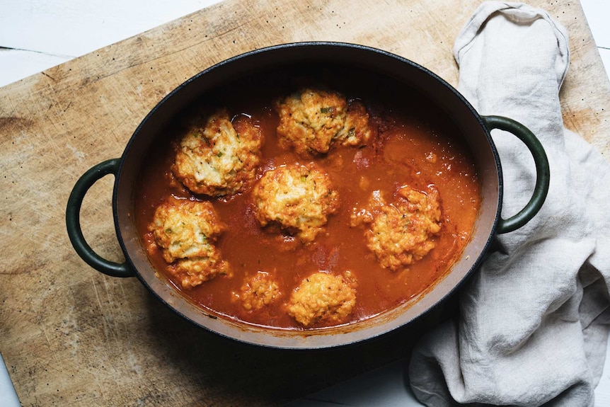 Fluffy spring onion dumplings cooking in a pot of smoky tomato soup.