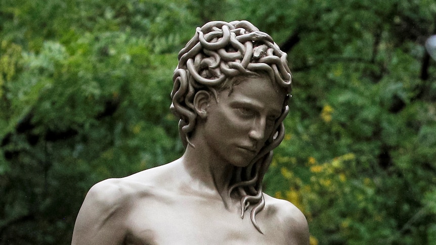 Two women take a selfie in front of a statue of a woman with snakes for hair 