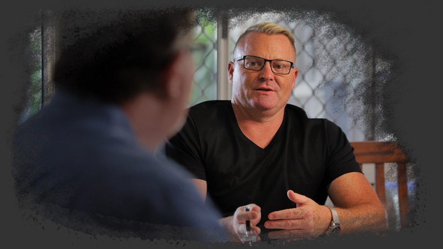 A middle aged man sitting at a kitchen table with another man.