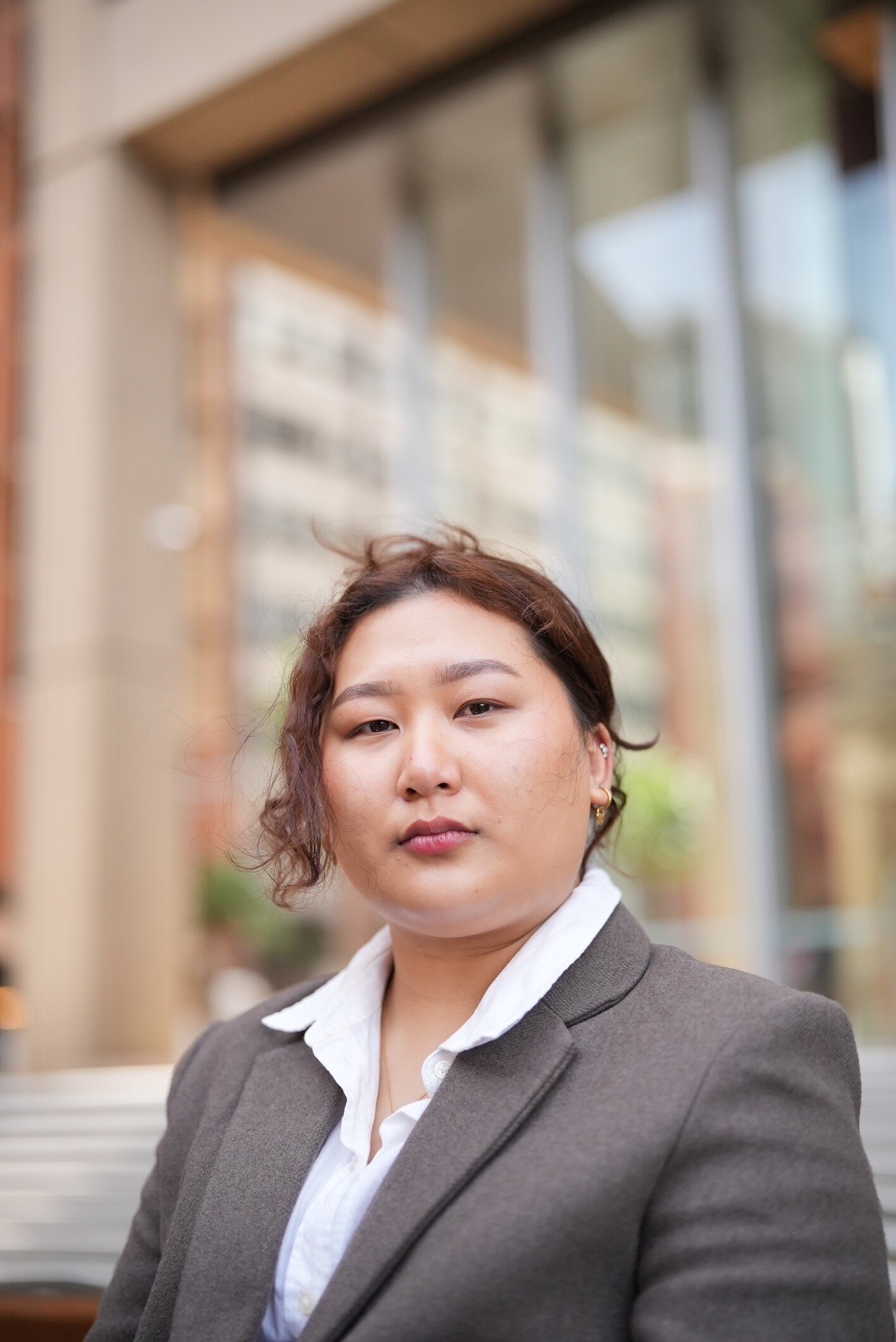 A woman in a suit looks down the barrel of the camera.