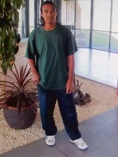 A young man wearing a green top and navy blue pants standing in a courtyard 