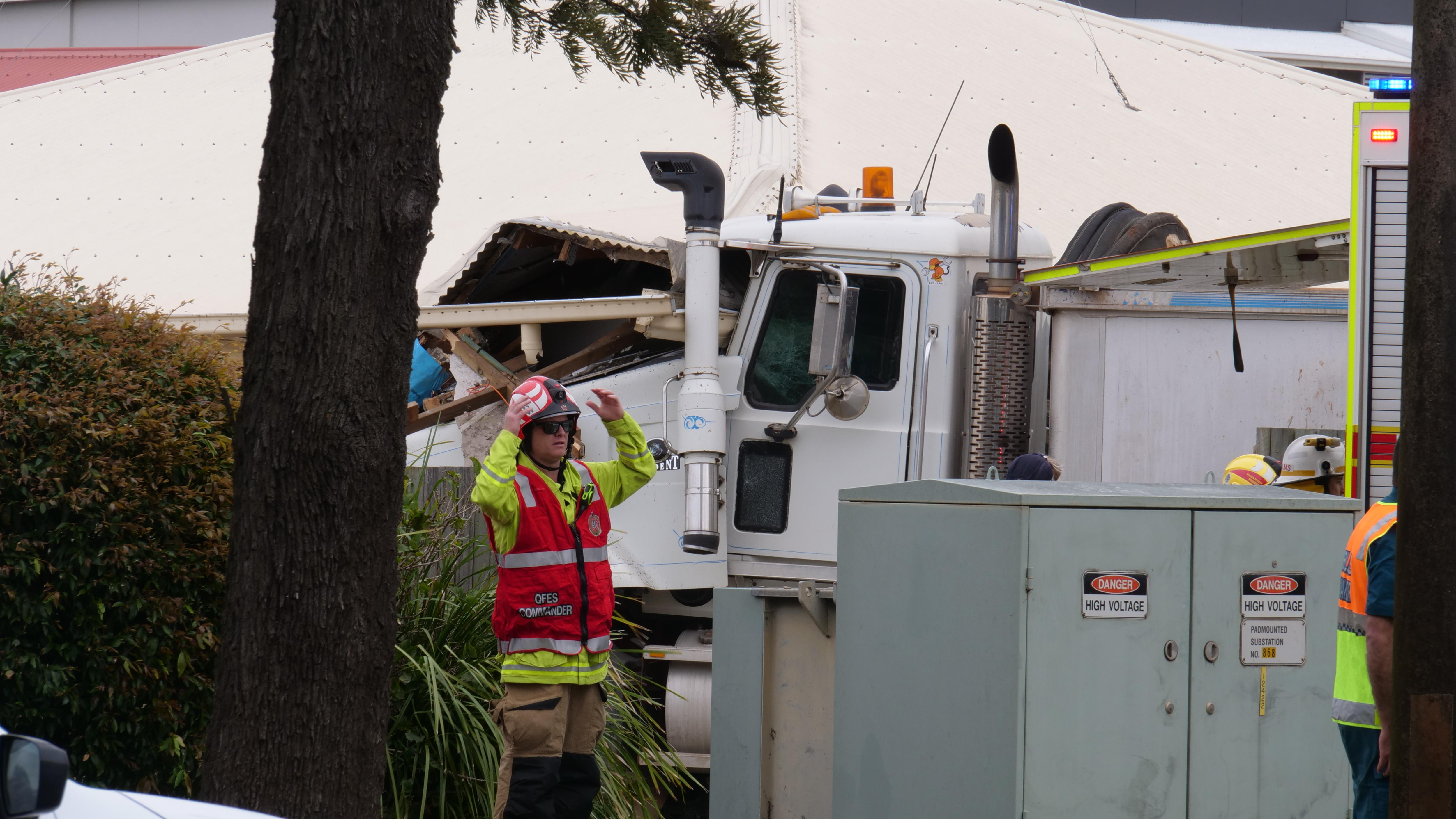 A fireman stands in front of a truck cab and damaged unit
