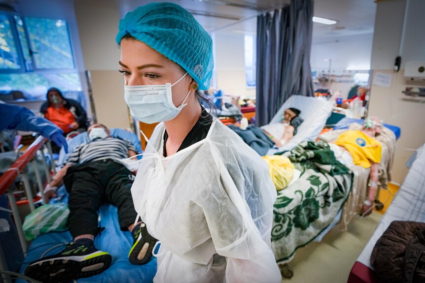 Une agente de santé portant un masque se tient au milieu de plusieurs lits d'hôpitaux contenant des patients COVID