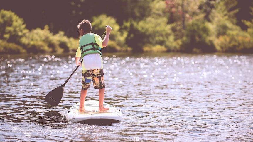 A boy wearing a life jacket on a stand-up paddle board.