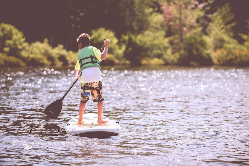 A boy wearing a life jacket on a stand-up paddle board.