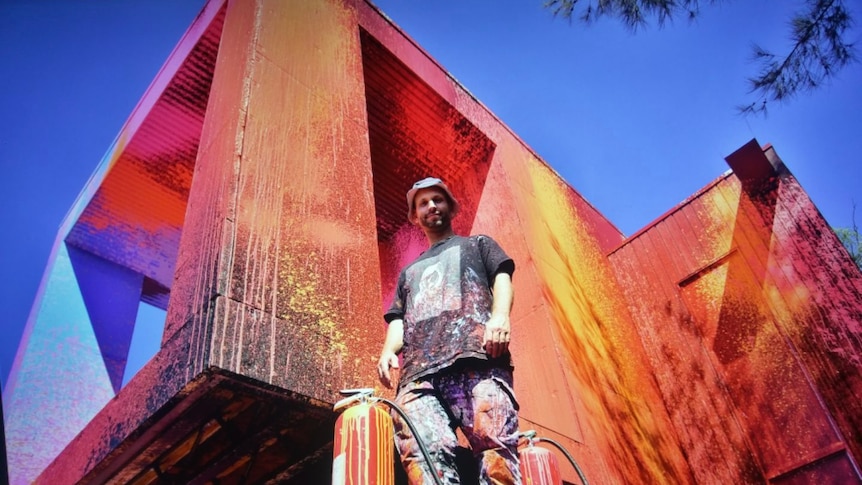 A man, Ash Keating, outside a very brightly coloured house