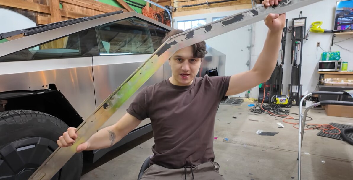 A man holds up a panel of a Cybertruck