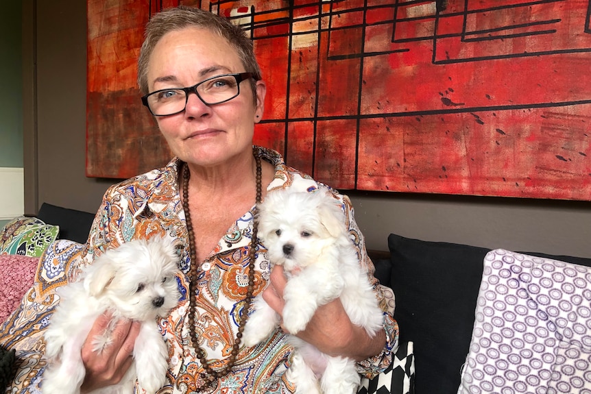 Lizi Hofer sits on couch holding two Maltese puppies