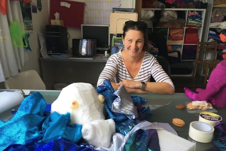 Woman sitting at a table smiling with a foam dragon head and bright material.